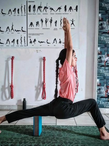 A student practices Virabhadrasana I (Warrior I Pose) with precise alignment, a foundational pose for strength and stability.