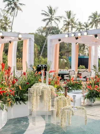 A poolside setup featuring elegant white and blush draped cabanas, accented with vibrant tropical flowers. The design includes unique floral installations floating in the water.