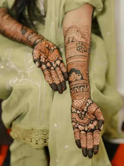 A beautiful shot of a bride's mehendi, with intricate patterns covering her hands and arms. The design is a mix of floral, peacock, and geometric motifs.