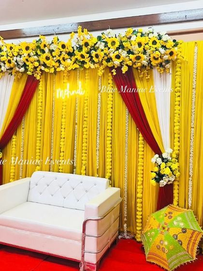 Another angle of the sunflower-themed Haldi/Mehendi decor, highlighting the 'Mehendi' neon sign and the layers of yellow drapes and marigold garlands.