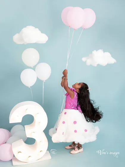 Floating into her third year. This whimsical birthday portrait features the birthday girl holding pink balloons, surrounded by fluffy clouds and a light-up number three.