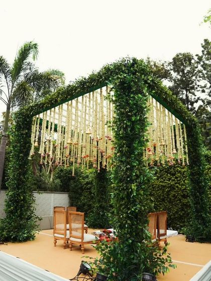 A unique wedding mandap with a frame covered in lush greenery. The ceiling is a cascade of hanging white floral strings with bells, creating a natural and serene ambiance.