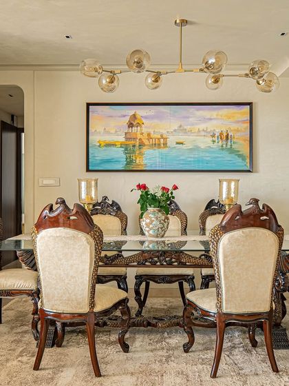The dining area from the 'Eternity' project, featuring an intricately carved traditional wooden dining set. The classic furniture is paired with a modern painting and chandelier for a balanced, eclectic look.