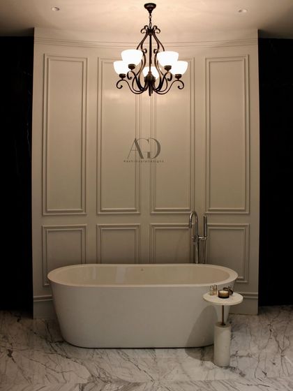 A minimalist approach to classic design. This bathroom features a simple, elegant freestanding tub set against a backdrop of clean, white paneled walls and a classic chandelier, proving that luxury can be understated.