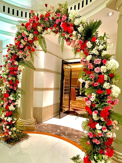 A magnificent floral arch in red, pink, and white stands at the entrance, creating a vibrant and joyful welcome for guests.