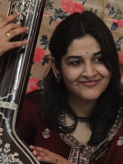 A student with her tanpura, the instrument that provides the foundational drone for all classical vocal music. Her smile reflects the joy of being part of the musical evening.