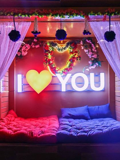 Here is a closer look at one of our romantic setups, complete with plush floor seating and an "I Love You" sign. It's designed to be a comfortable and intimate space for you and your partner to relax.