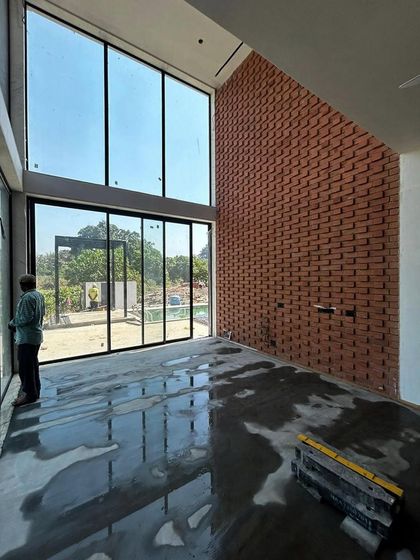 The double-height living space at a Kolgaon villa during construction. The exposed brick feature wall and large window apertures are visible, showing how we integrate materials and light from the very beginning of the building process.