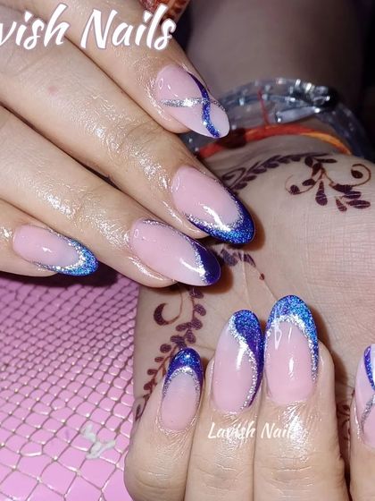 Elegant almond nails with a deep blue glitter French tip and silver glitter criss-cross accents, shown against a hand with mehendi.