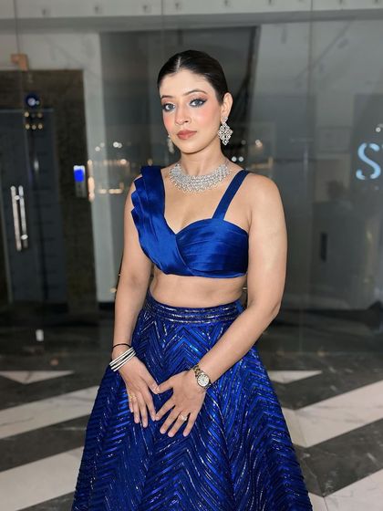 A full portrait of the client in her blue outfit. The sleek hair and bold outfit are balanced by the classic, clean makeup.