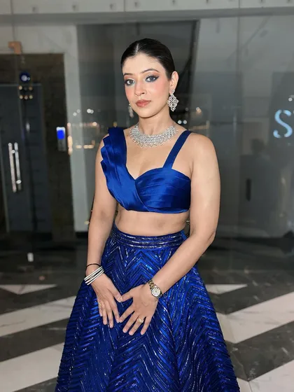 A full portrait of the client in her blue outfit. The sleek hair and bold outfit are balanced by the classic, clean makeup.