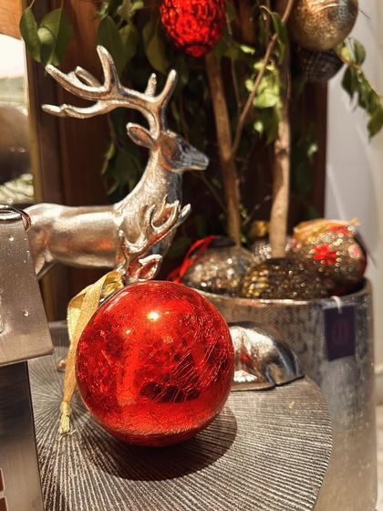 A close-up of a bright red Christmas bauble next to a silver reindeer, capturing the classic colors and textures of the holiday season.