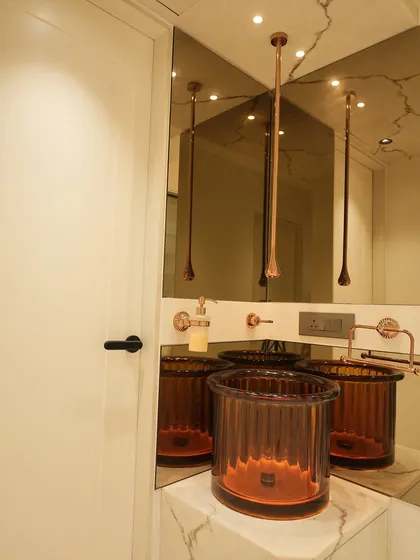 We believe luxury is in the details. This unique amber glass washbasin, paired with rose gold fixtures and a tinted mirror, creates a stunning focal point in the powder room, showcasing our commitment to bespoke design.