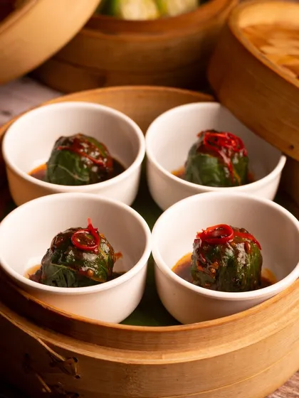 Steamed dumplings in individual serving bowls, garnished with chili. The presentation is elegant and the close-up shot makes them look very appetizing.