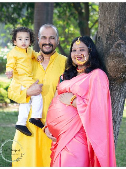 A growing family portrait, with a mother in a pink saree and traditional jewelry, her husband, and their young son in a matching yellow kurta. This maternity shoot celebrates the arrival of a new member.