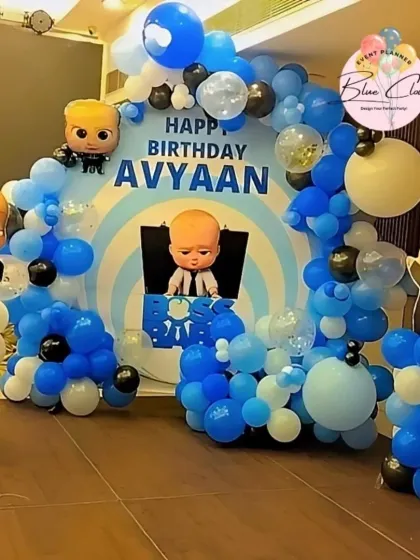 A fun Boss Baby themed birthday decoration. This setup includes a custom circular backdrop with character cutouts and a blue, black, and white balloon garland.