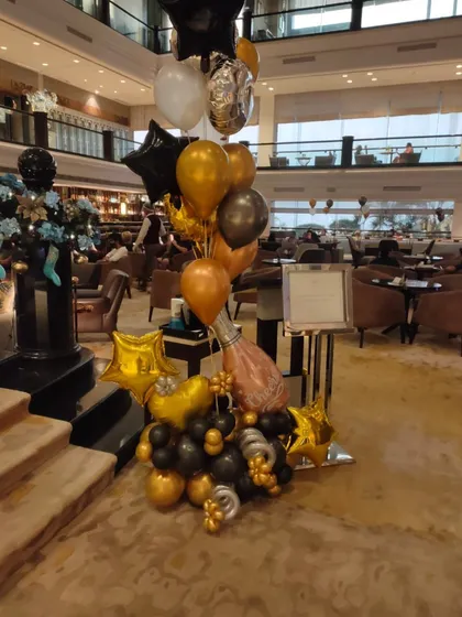A stylish balloon arrangement for a corporate event or party. This bouquet combines black, gold, and silver balloons with star-shaped foils and a champagne bottle foil for a celebratory touch.
