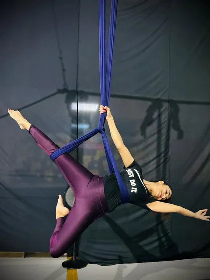 A student strikes a powerful pose, extending her body to create a beautiful line. This demonstrates the core strength gained through aerial silk training.