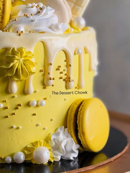 A close-up of a vibrant yellow birthday cake with a white chocolate drip, macarons, and delicate piping. This was a red velvet cake inside.