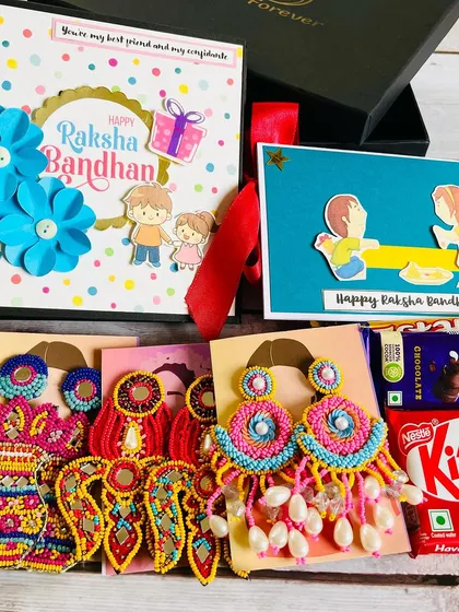 This is what a box of happiness looks like! A perfect Rakhi gift hamper for a sister, featuring a handmade album for memories, chocolates, and a pair of our vibrant, festive mirror-work earrings.