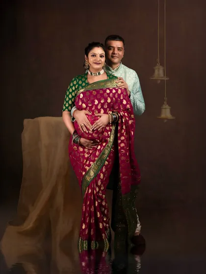A traditional and elegant couple portrait. The clients are dressed in beautiful Indian attire, creating a culturally rich and sophisticated image against a classic studio backdrop with temple bells.