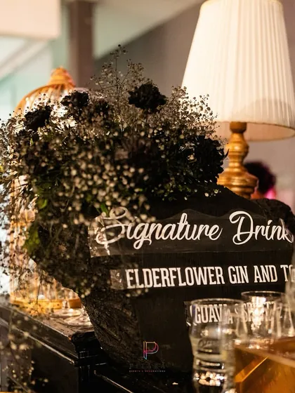 The signature drink menu for the event, displayed on a custom acrylic sign. The bar was decorated with black baby's breath and a modern table lamp, tying into the moody and chic theme.