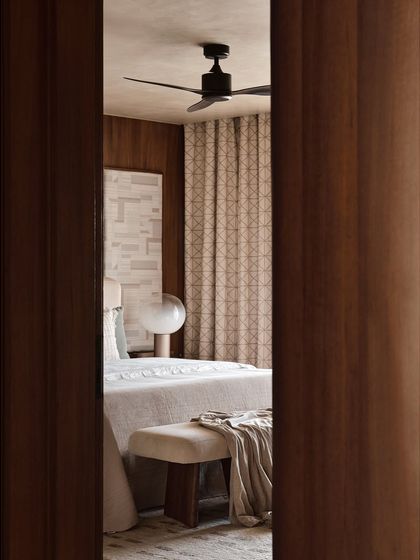 Peeking into a bedroom, this view highlights the layering of textures and patterns. The geometric-print curtains and soft textiles on the bed create a warm and inviting atmosphere, consistent with our modern organic style.