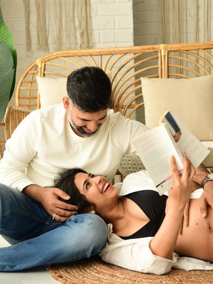 A candid and joyful moment from a casual boho session. The couple is relaxing on the floor, sharing a laugh over a book, surrounded by the warm and natural elements of the set.