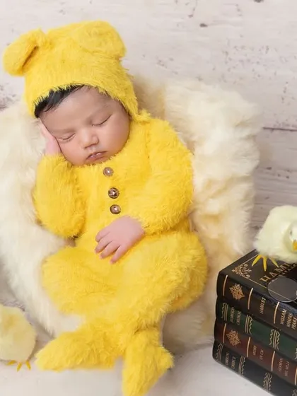 Dressed in a fuzzy yellow teddy bear outfit, this newborn is just adorable.
