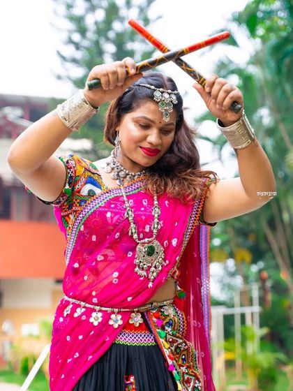 A powerful and energetic pose during a Navratri dandiya shoot. Dressed in a bright pink and black ghagra choli, she holds her dandiya sticks high, ready to dance, embodying the spirit of the festival.