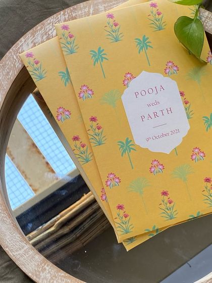 A bright and cheerful invitation folder with a yellow background and a pattern of pink block-print style flowers and palm trees. This design is perfect for a fun, daytime wedding.
