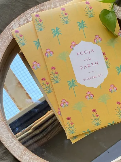 A bright and cheerful invitation folder with a yellow background and a pattern of pink block-print style flowers and palm trees. This design is perfect for a fun, daytime wedding.