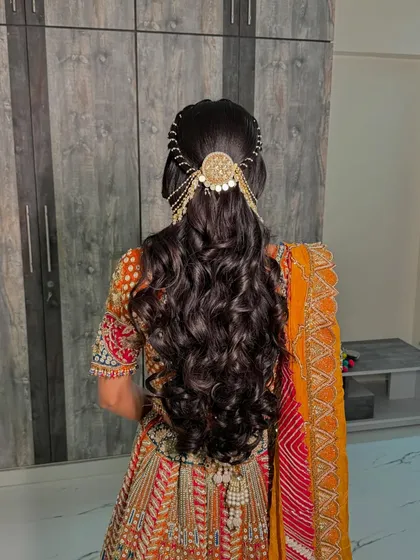 A hairstyle fit for a queen. This intricate half-updo features a stunning traditional hair accessory, adding a regal touch to her vibrant engagement lehenga.