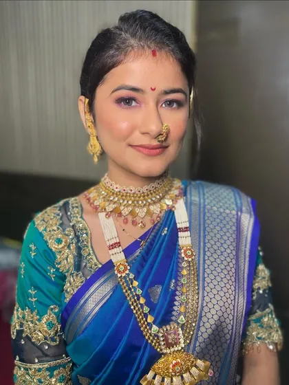 A beautiful bride in a royal blue saree. The makeup is soft and glowing, with a traditional 'nath' and 'chandrakor' bindi completing the look.
