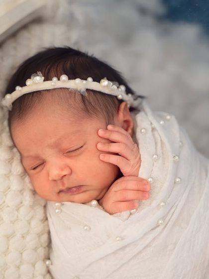 A close-up of a little angel, swaddled in a white wrap with pearl details that match her delicate headband.