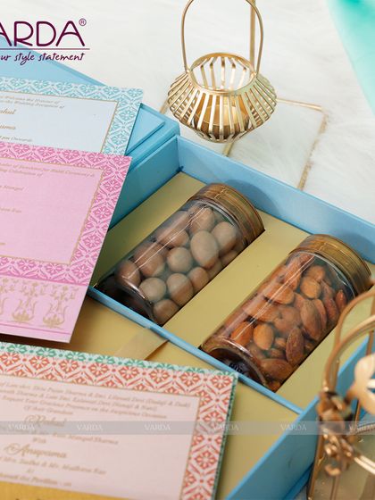 A lovely pastel blue gift box containing two large jars of premium almonds. This hamper is paired with a set of matching invitation cards in shades of pink, blue, and orange, creating a soft and elegant aesthetic.