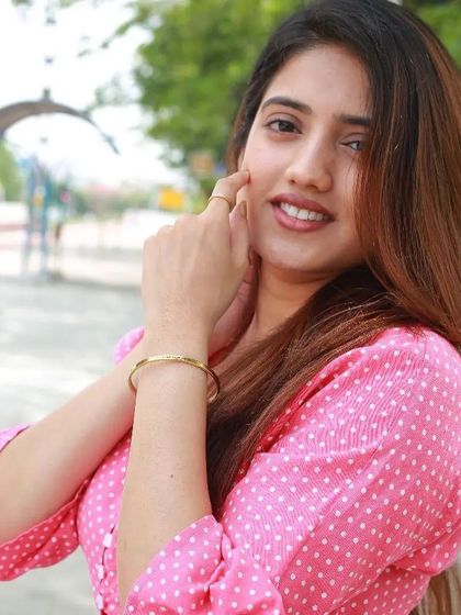 Another view of the woman in pink, touching her face and showing off the delicate gold cuff on her wrist.