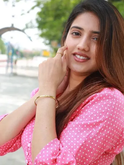 Another view of the woman in pink, touching her face and showing off the delicate gold cuff on her wrist.