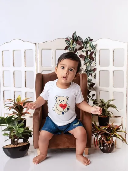 A charming baby portrait session with a simple, clean setup featuring a miniature chair and indoor plants for a touch of green.
