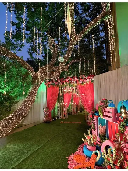The entrance to a colorful Mehndi party. The walkway is lit by a tree wrapped in fairy lights, leading into a space filled with vibrant decor and festive energy.