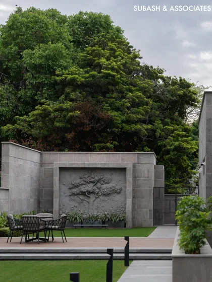 The side lawn features a custom stone relief sculpture of a tree, creating a serene focal point for this outdoor seating area.