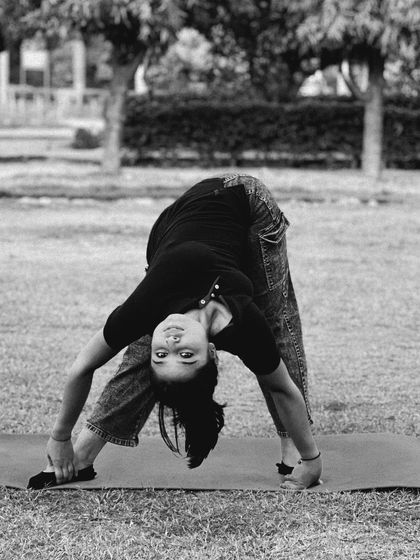 A student performs Prasarita Padottanasana (Wide-Legged Forward Bend) outdoors. This black and white shot emphasizes the form and deep stretch required for this foundational but challenging pose.