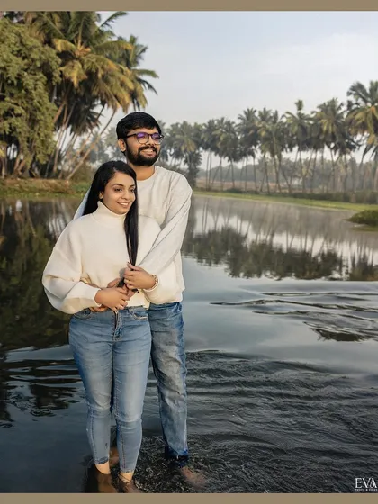 Standing in the calm river, Amrutha and Varun share a quiet embrace, with the lush landscape reflecting in the water around them.