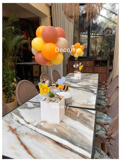 A themed table centerpiece for the 'Parents to Bee' shower, featuring a balloon arrangement in theme colors and a small bee prop.
