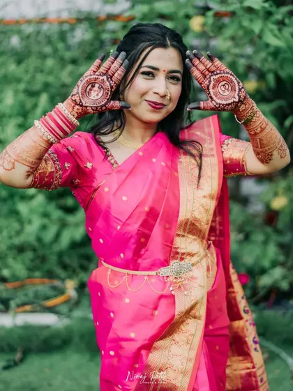 A beautiful bride posing with her engagement mehendi, which features circular frames on the palms for a portrait and wedding rings.