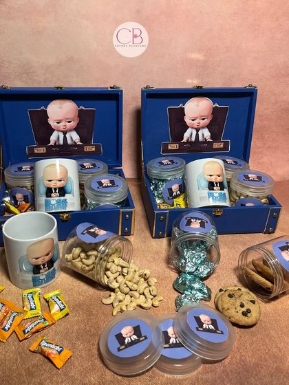 Our "Boss Baby" themed return favours are a top seller. This image shows the contents of our luxury trunk box version, including a custom mug and jars of cashews, cookies, and chocolates.