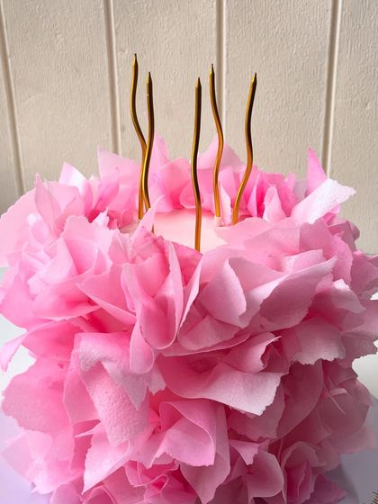 A bloom you can eat. A close-up of the edible pink ruffle cake, showing the layers of delicate petals and the elegant gold candles.