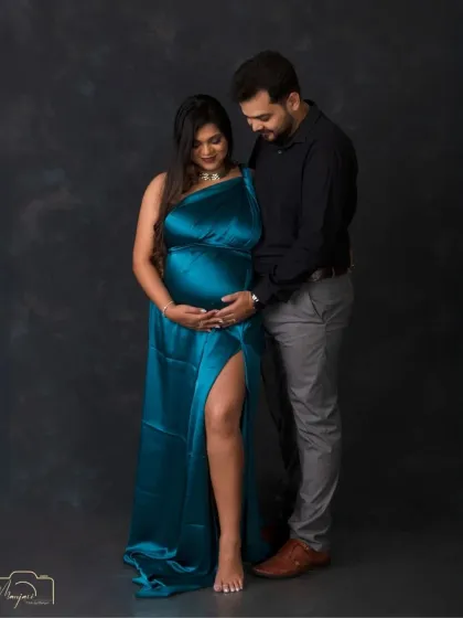A classic couple's portrait against a simple, dark background. The focus is entirely on their connection and the beautiful baby bump.