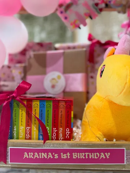 A cuddly unicorn plush toy next to a set of educational books, combining fun and learning in this first birthday gift.