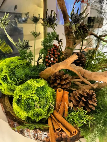 An earthy and aromatic display. This rustic centerpiece blends natural elements like moss balls, pinecones, and driftwood with the warm, spicy fragrance of cinnamon, providing a feast for the senses.